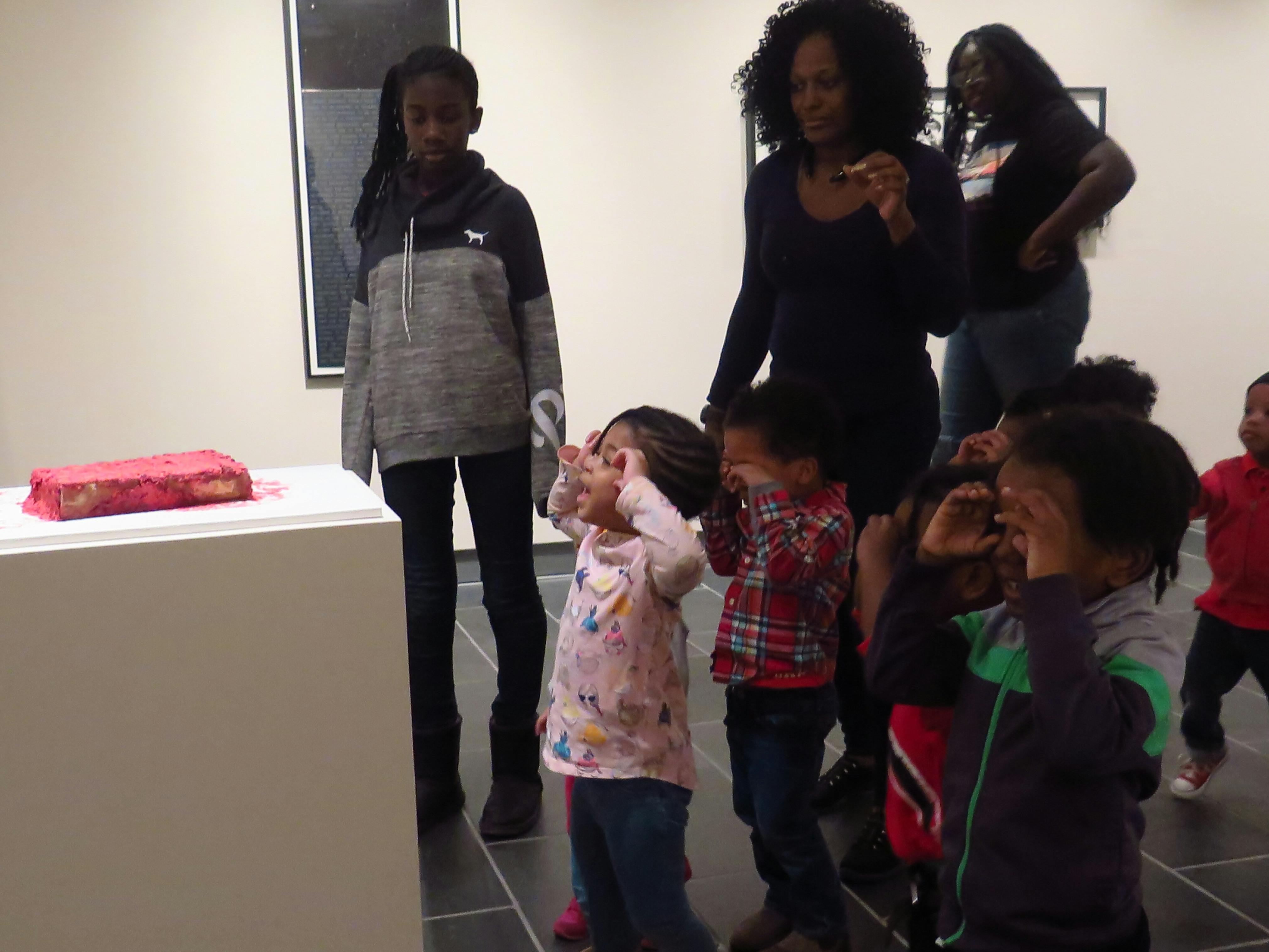 A group of children look at artwork in a gallery with white walls.