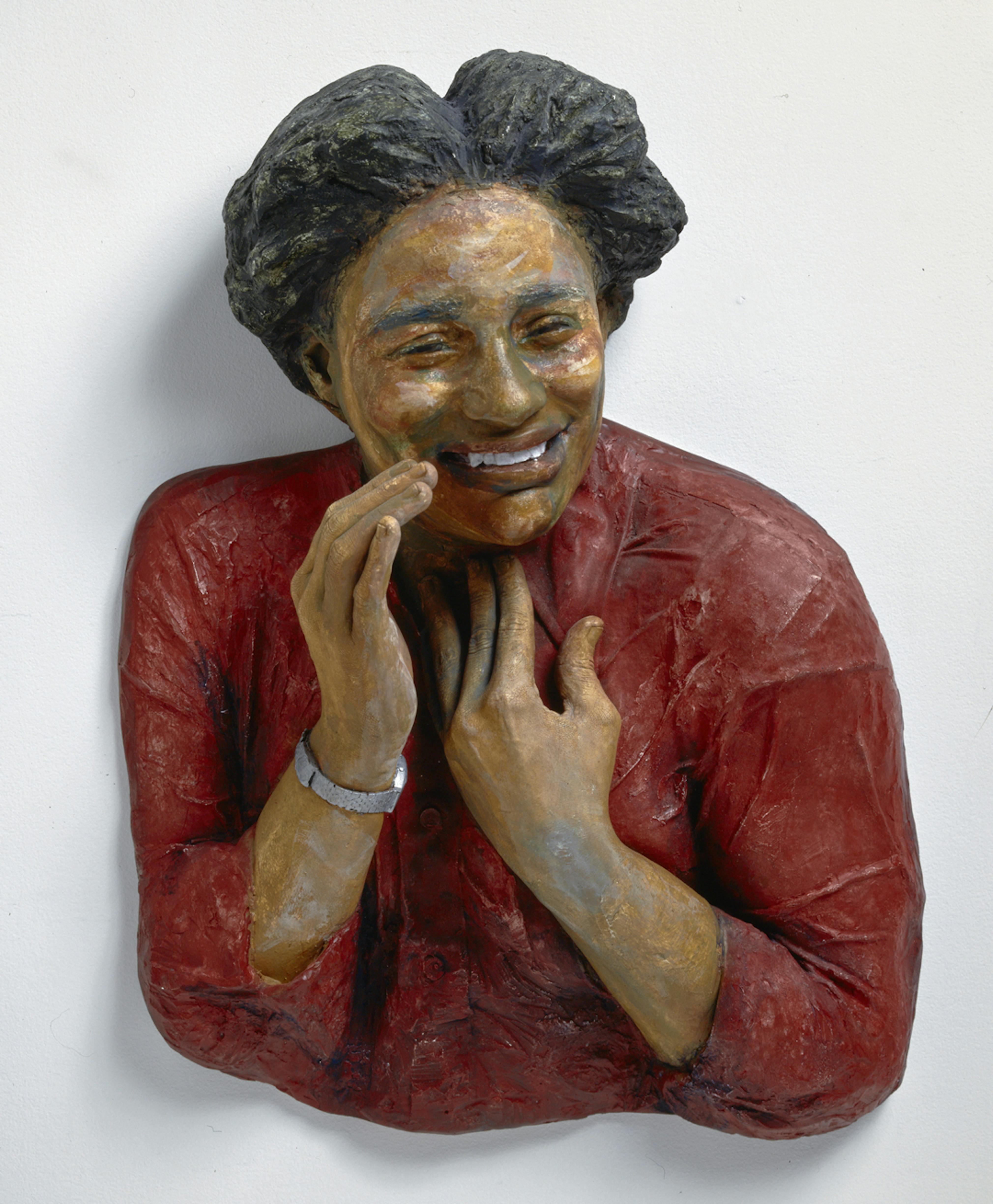 A plaster cast bust of a woman wearing a red shirt whose face is slightly turned, with a laughing smile she holds one hand up to her mouth as if calling to someone and holds her other hand to her chest.