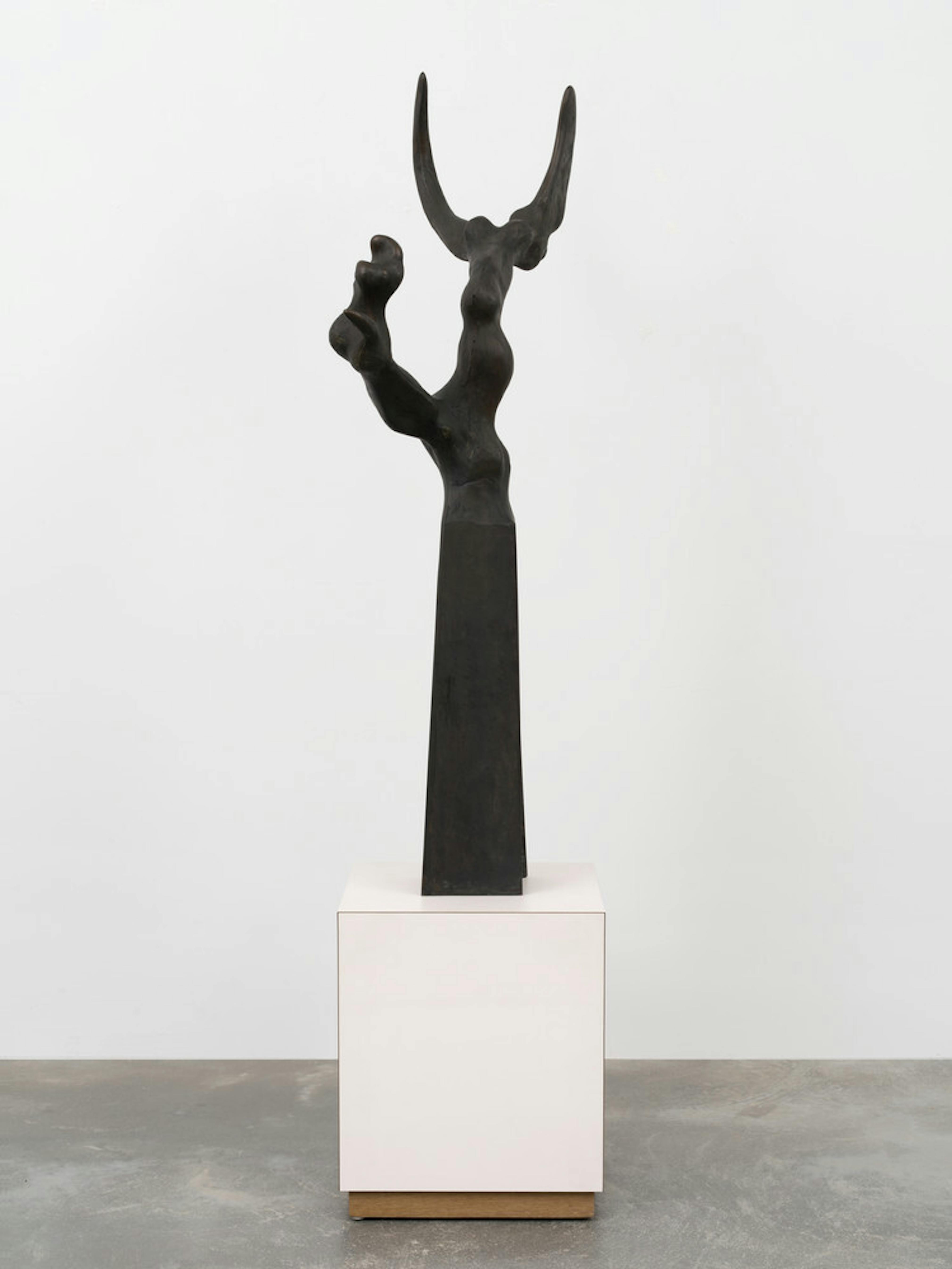 A black bronze sculpture with a geometric base that tapers upward into a slender biomorphic form that comes to two points like bull horns.