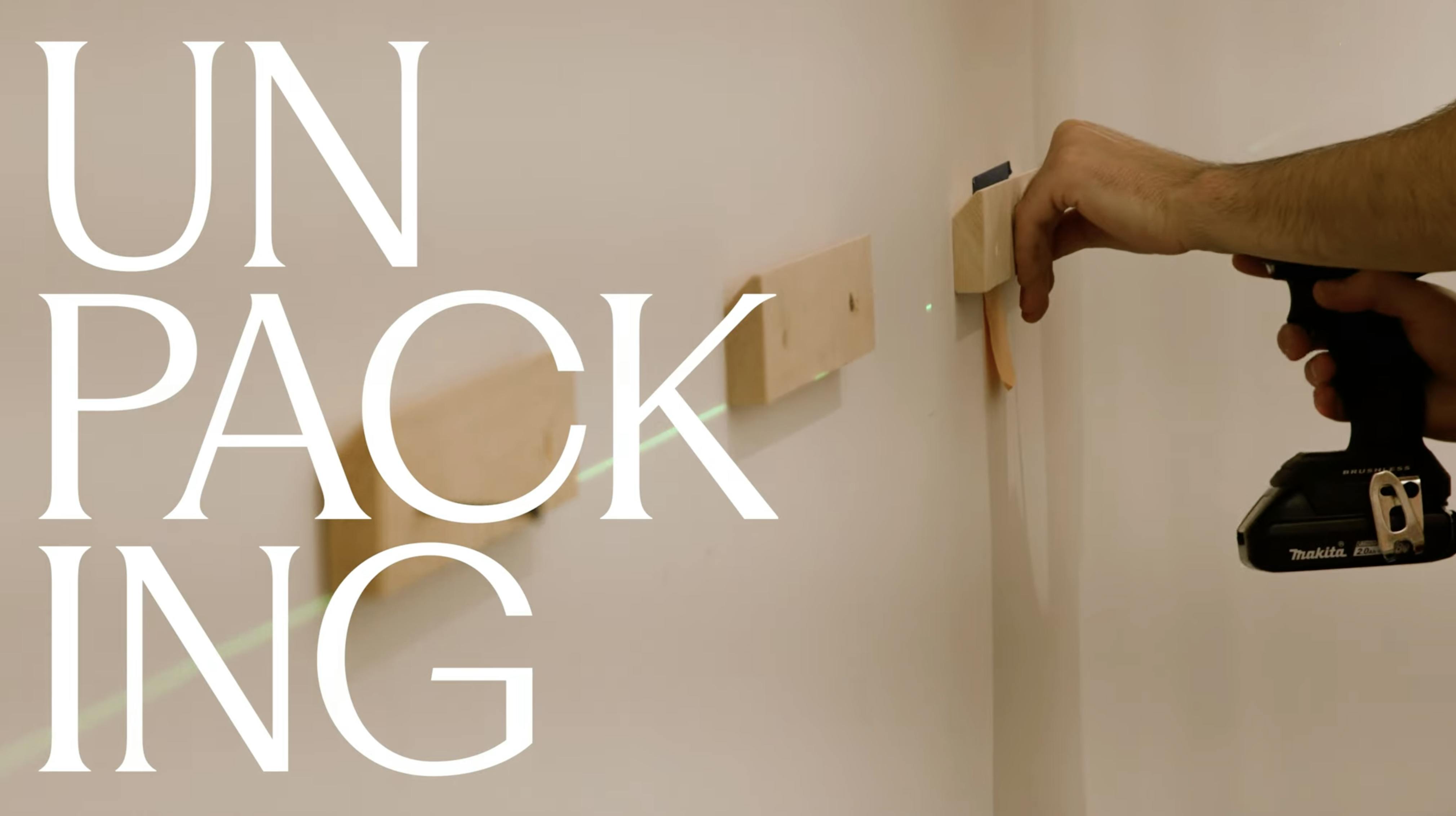 A hand with a drill working on wood panels on a white wall.