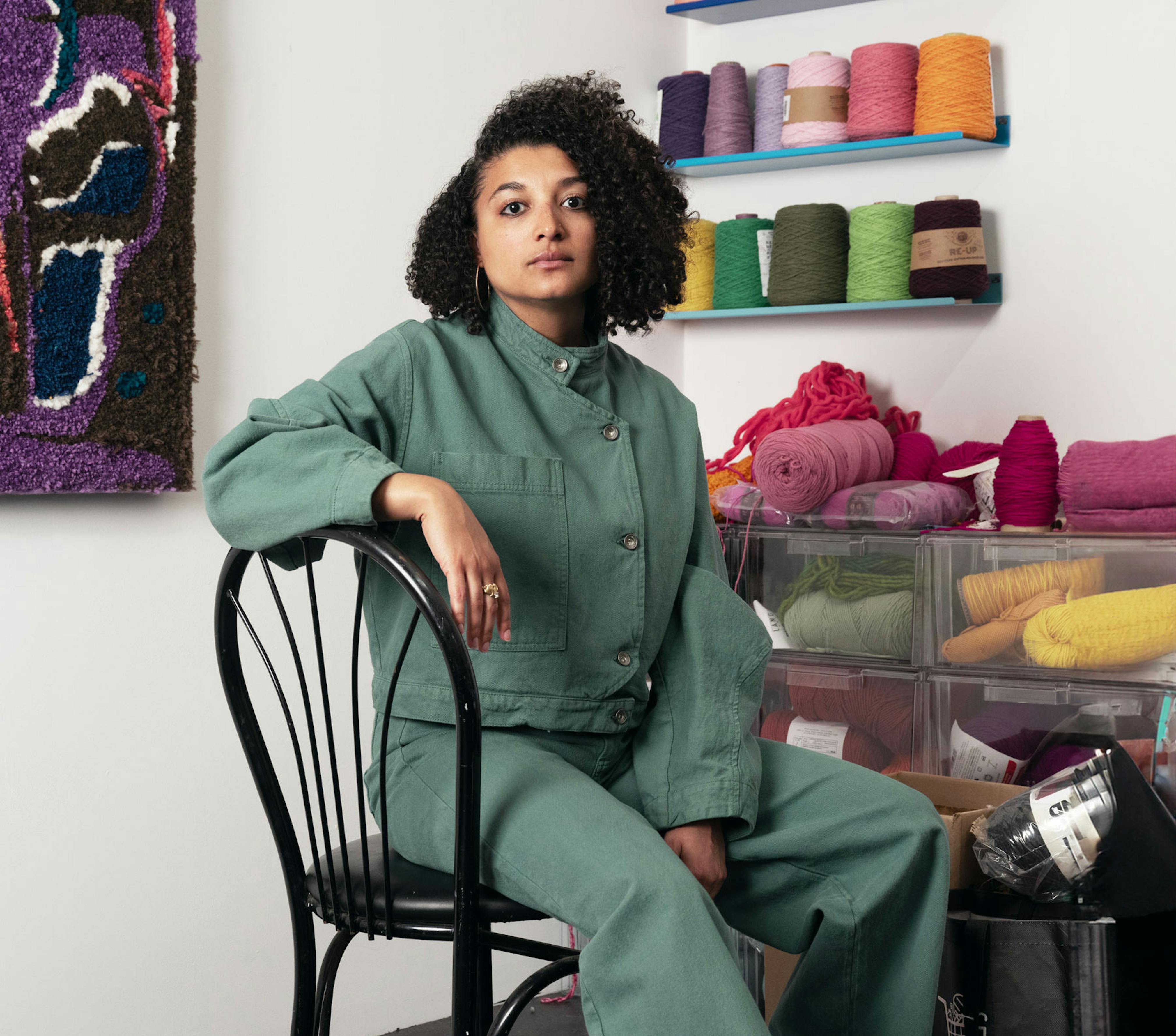 A light brown-skinned person sits in a chair surrounded by colorful yarn.